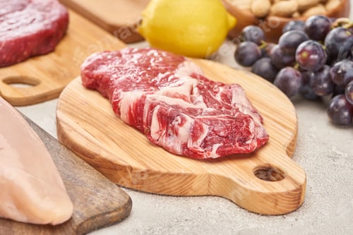 Preview: Raw mmeat tenderloin on wooden cutting board near grapes and lemon on marble surface