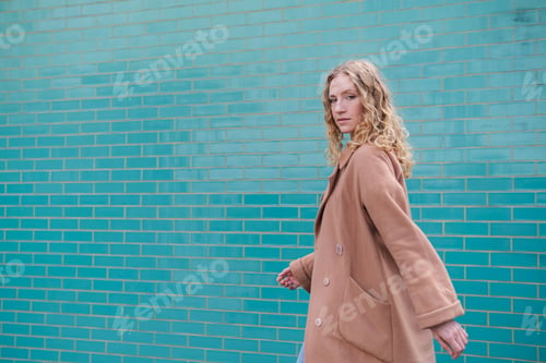 Preview: Woman in Long Coat Walks with a Defiant Gaze Against a Brick Wall