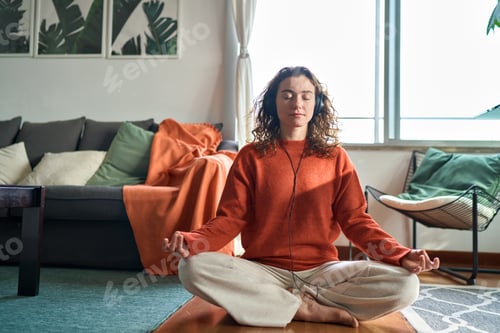 Preview: Young calm woman wearing headphones doing yoga meditation at home.