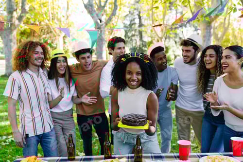 Visualização: Mulher segurando bolo de aniversário comemorando com amigos na festa ao ar livre