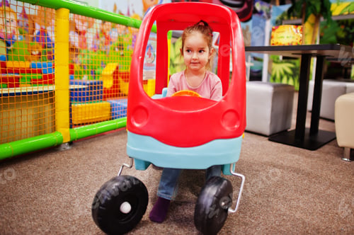Preview: Cute baby girl rides on a plastic car in indoor play center.