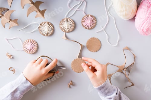Preview: Children's hands cut cardboard circles for DIY Christmas handmade decorations. Top view.