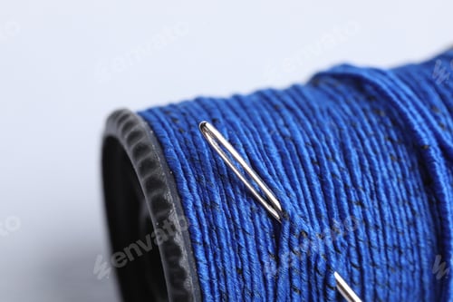 Preview: Spool of blue thread with needle on grey background, closeup