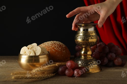 Preview: Cup in hand, bread, spikelets, grapes on wooden table on black background