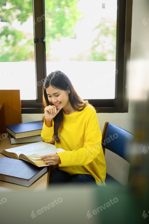 Preview: Smiling asian female student reading book, doing class assignment. in library.