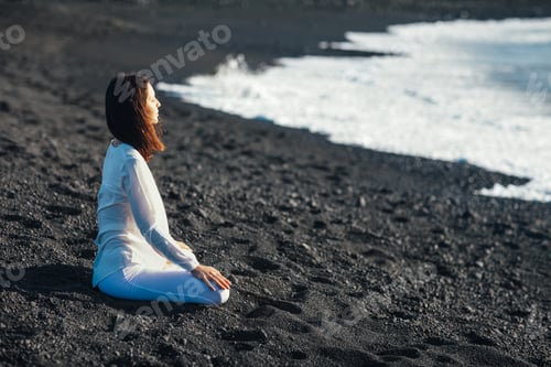 Preview: Young woman meditating in Lotus Pose in black sand beach in Lanzarote, Canary Islands, Spain