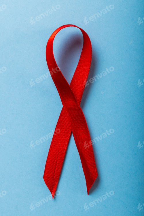 Preview: Overhead close-up of red aids awareness ribbon isolated against blue background, copy space