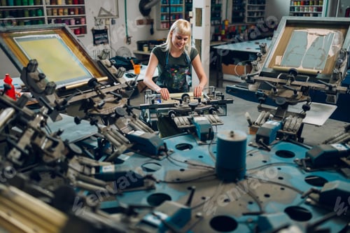 Preview: Female graphic worker with squeegee is screen printing at print shop.