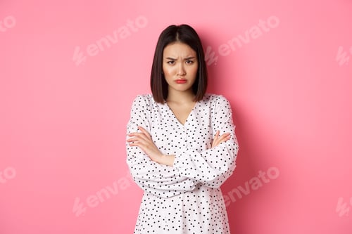 Preview: Timid and offended asian girl cross arms on chest, staring defensive and insulted at camera