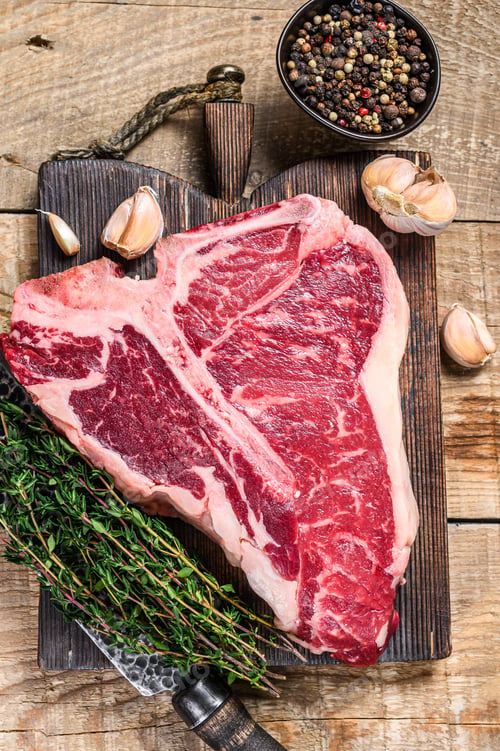 Preview: Raw Porterhouse or T-bone beef meat Steak with herbs on a wooden cutting board.