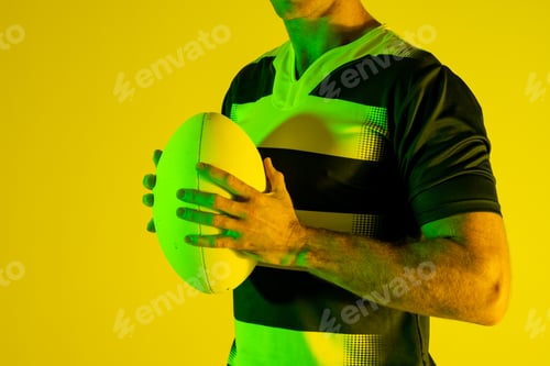 Preview: Caucasian male rugby player with rugby ball over orange lighting