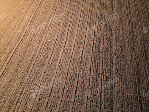 Preview: Freshly plowed soil with evenly spaced furrows, creating a textured pattern across the surface. The