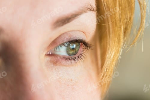 Preview: Closeup of the green eye of a blonde woman with a blurry background