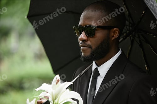 Preview: Black Man in Sunglasses Grieving under Umbrella during Funeral at Cemetery