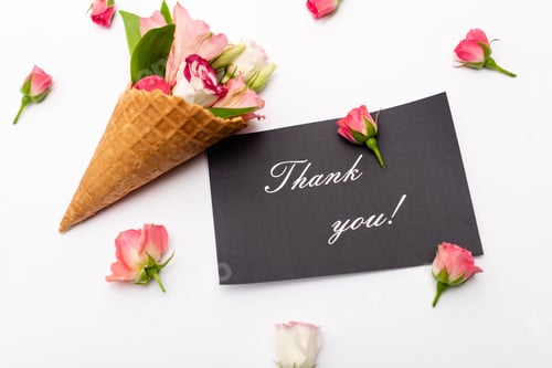 Preview: top view of pink flowers in waffle cone near card with thank you lettering on white