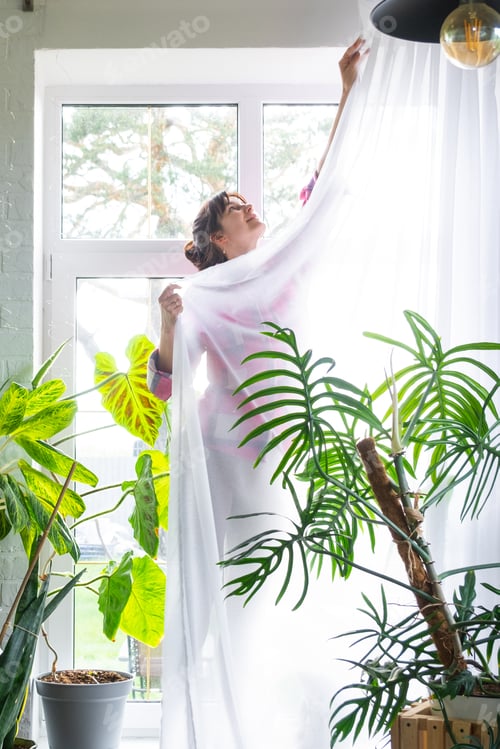 Preview: Woman hangs transparent tulle curtains on large windows in the house inside the interior. Spring cle
