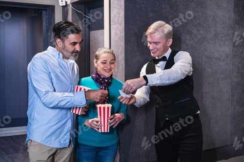Preview: Usher checking tickets of couple eating popcorn at movie theater