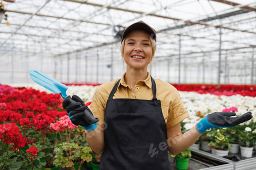 Preview: Joyful female worker of a flower greenhouse with a hand trowel in her hands