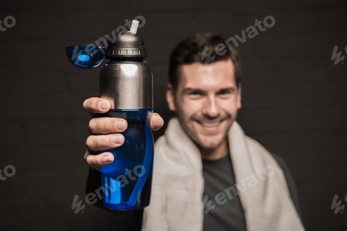 Preview: Close-up portrait of handsome man with towel on shoulders, holding bottle in hand