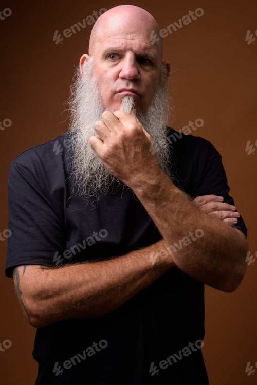 Preview: Mature bald man with long gray beard against brown background