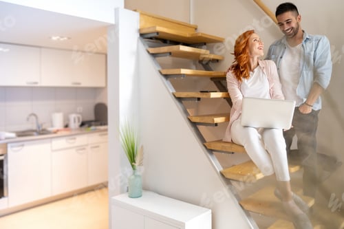 Aperçu: Cute, young and happy couple using laptop together on the stairs at home.