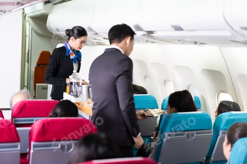 Preview: Asian female and male flight attendant serving food and drink to passengers on airplane.