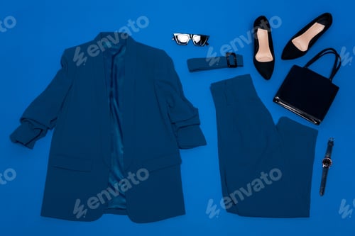 Preview: top view of jacket, trousers, heels, belt, bag, wristwatch and sunglasses isolated on blue
