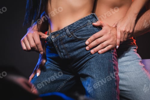 Preview: partial view of man hugging hips of woman in jeans on blurred foreground isolated on black