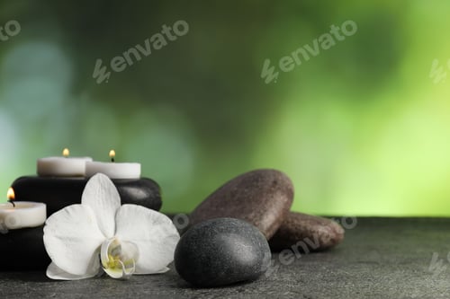 Preview: Spa stones, burning candles and orchid flower on grey table, closeup. Space for text