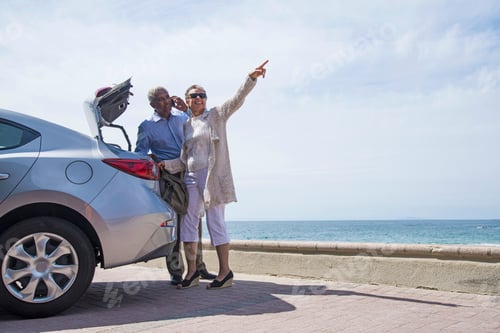 Preview: Senior couple standing beside car with open boot, near beach