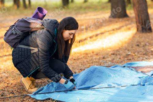 Preview: Young woman setting tent in camp, backpacking at countryside