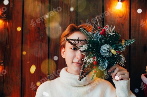 Preview: Teenage girl covering her face with christmas star and smiling