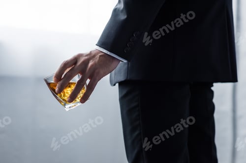 Preview: partial view of man in black suit holding glass of whiskey