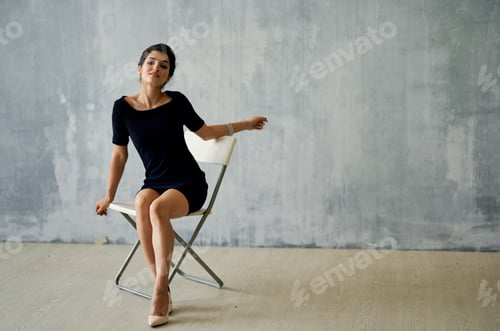 Preview: sexy brunette with a bracelet on her arm sits on a chair indoors