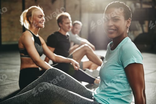 Preview: Smiling young woman sitting with friends on a gym floor