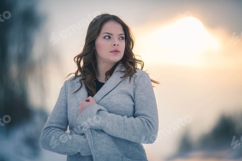 Preview: Shallow focus of a young woman wearing a gray coat and posing in a forest covered in the snow