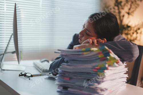 Preview: Exhausted office worker sleeping on stack of documents at desk