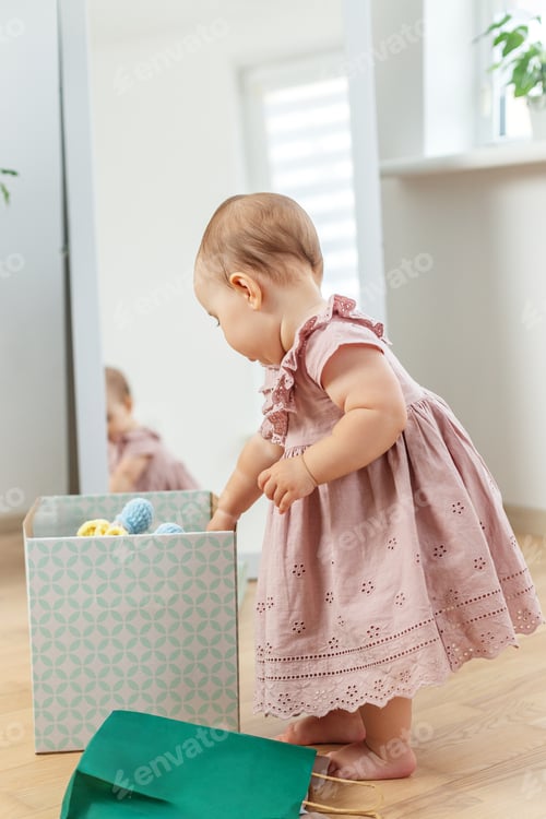 Preview: Baby Girl Standing and Exploring Toy Box at Home – Early Development Concept