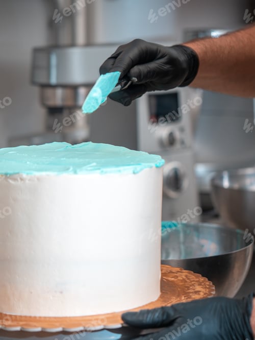Preview: cake designer covering a frosted blank cake with turquoise light blue cream with spatula