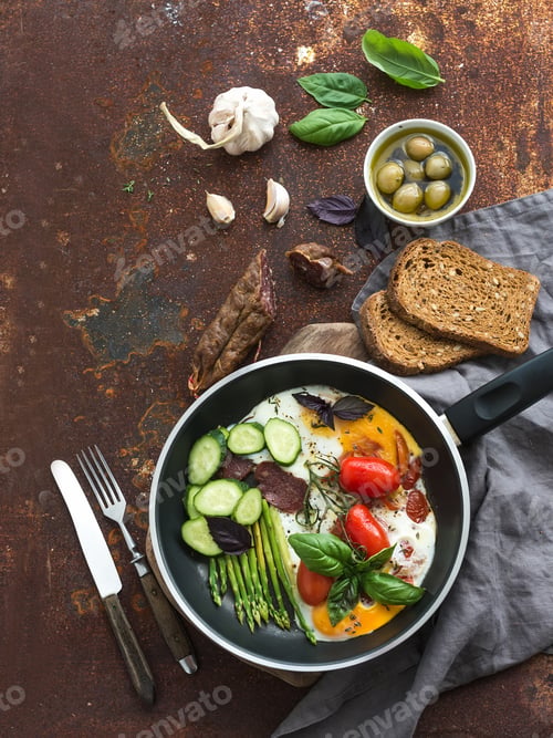Preview: Pan of fried eggs, salami, asparagus, cherry-tomatoes with bread, fresh basil, olives and garlic