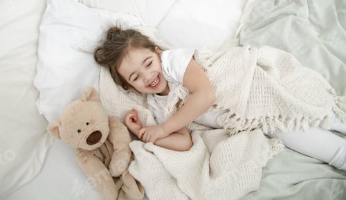 Preview: A cute little girl is sleeping in a bed with a Teddy bear toy .