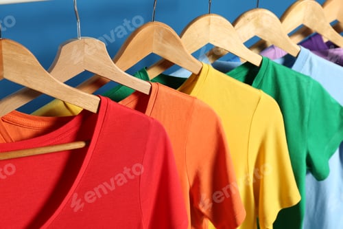 Preview: Bright clothes on wooden hangers against blue background, closeup. Rainbow colors