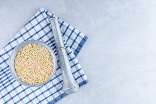 Preview: Folded towel underneath a herb masher and a metal jug of brown rice on marble background