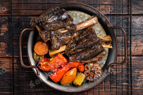 Preview: Homemade Braised Lamb Shanks with Sauce and Herbs in a steel tray. Wooden background. Top view