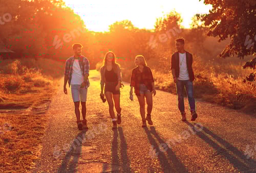 Preview: Group of four friends having fun hiking through countryside together on road during sunset.