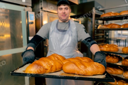 Preview: close up In a professional kitchen an inclusive baker stands with ready-made bread on a tray smiling