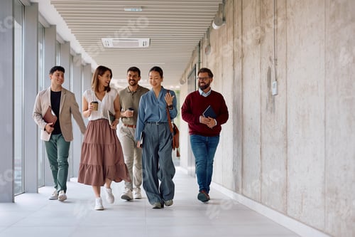 Preview: Happy colleagues talking while walking through office hallway.