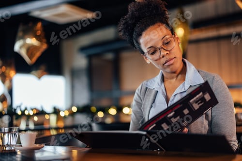 Preview: Serious african-american businesswoman, looking for a tasty dessert to eat at a pastry shop.