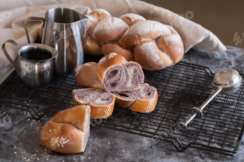 Preview: Purple baked challah on a black grill. Metal jugs and sieve. Bread.