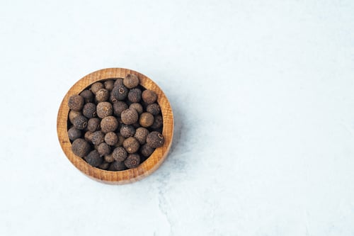 Preview: Whole black peppercorns in a wooden bowl on a marble surface